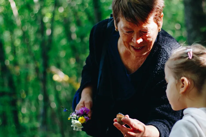 A grandmother showing wildflowers to her granddaughter in the woods